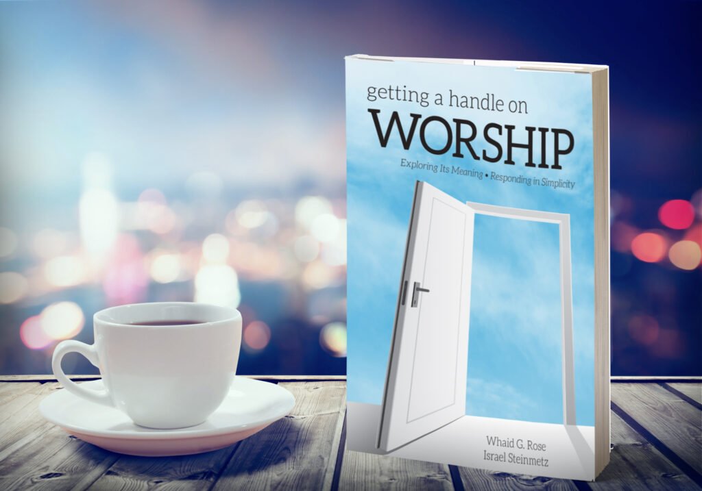 cover mock up English copy A book titled Getting a Handle on Worship next to a cup of coffee on a wooden table with blurred city lights.