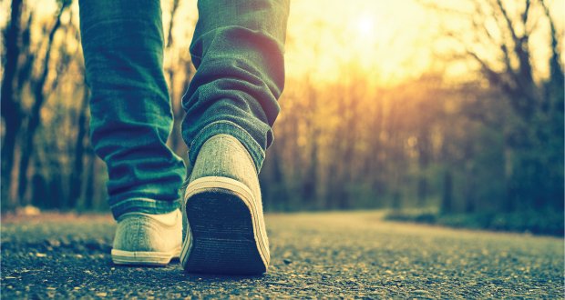 Person walking on a sunlit path in casual jeans and sneakers, symbolizing journey and exploration.